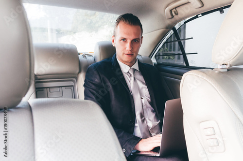Handsome businessman working on laptop computer sitting on back seat of a car © Art_Photo
