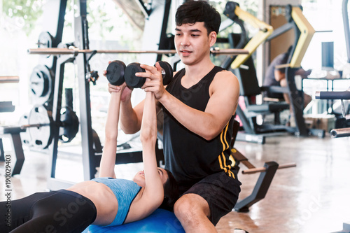 Handsome trainer and fitness woman with weight training equipment at the gym.fitness and lifestyle concept