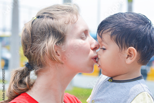 Young caucasian mother comforting and kissing her little sad latin son.