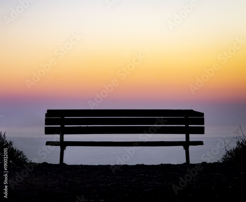 Old wooden bench overlooking a colorful sunset above the foggy ocean horizon