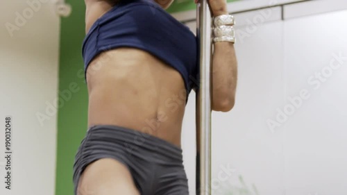 Afroamerican pole dancer is preparing for the show training the main elements. Lady is turning upside-down in v invert and tuck hip hold poses. Woman is wearing blue sportswear and silver accessories