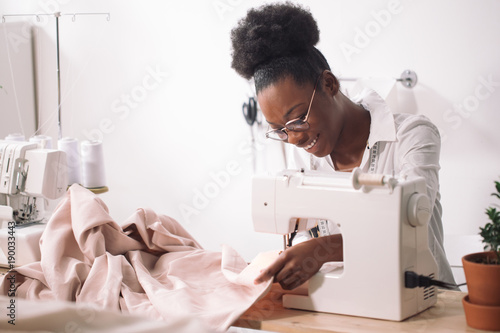 african seamstress sews clothes. Workplace of tailor - sewing machine, rolls of thread, fabric, scissors. photo