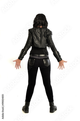 full length portrait of black haired girl wearing leather outfit. standing pose view from behind, on a white background