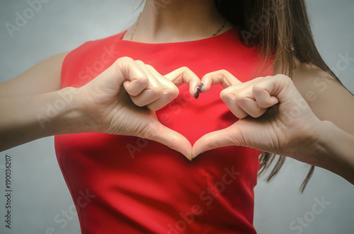 Love heart. Girl is holding hands in the shape of heart on a background of red dress.