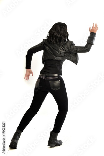full length portrait of black haired girl wearing leather outfit. standing pose view from behind, on a white background