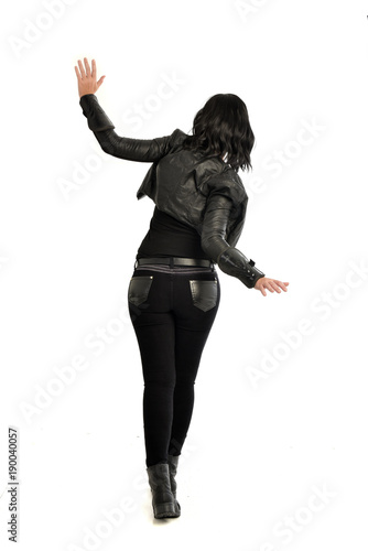full length portrait of black haired girl wearing leather outfit. standing pose view from behind, on a white background