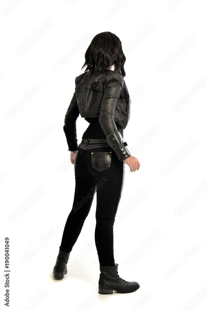 full length portrait of black haired girl wearing leather outfit. standing pose  view from behind, on a white background