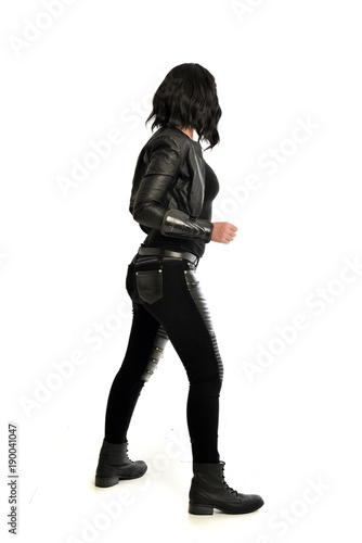 full length portrait of black haired girl wearing leather outfit. standing pose view from behind, on a white background