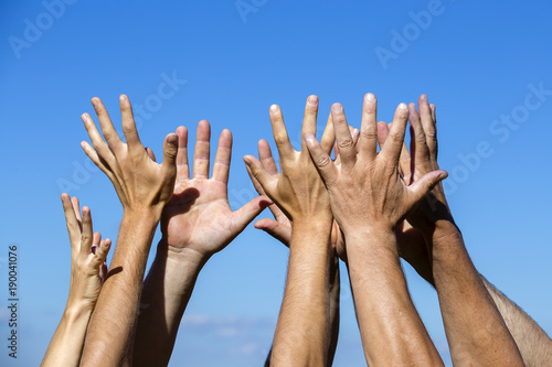Group raising hands against blue sky background, close up