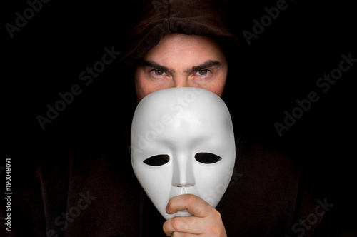 Mysterious man in black hiding his face behind white mask