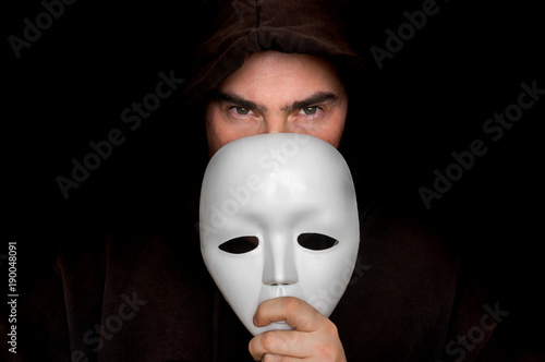 Fotografie Mysterious man in black hiding his face behind white mask