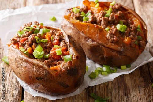 Homemade baked sweet potato stuffed with beef meat and green onions close-up on the table. horizontal