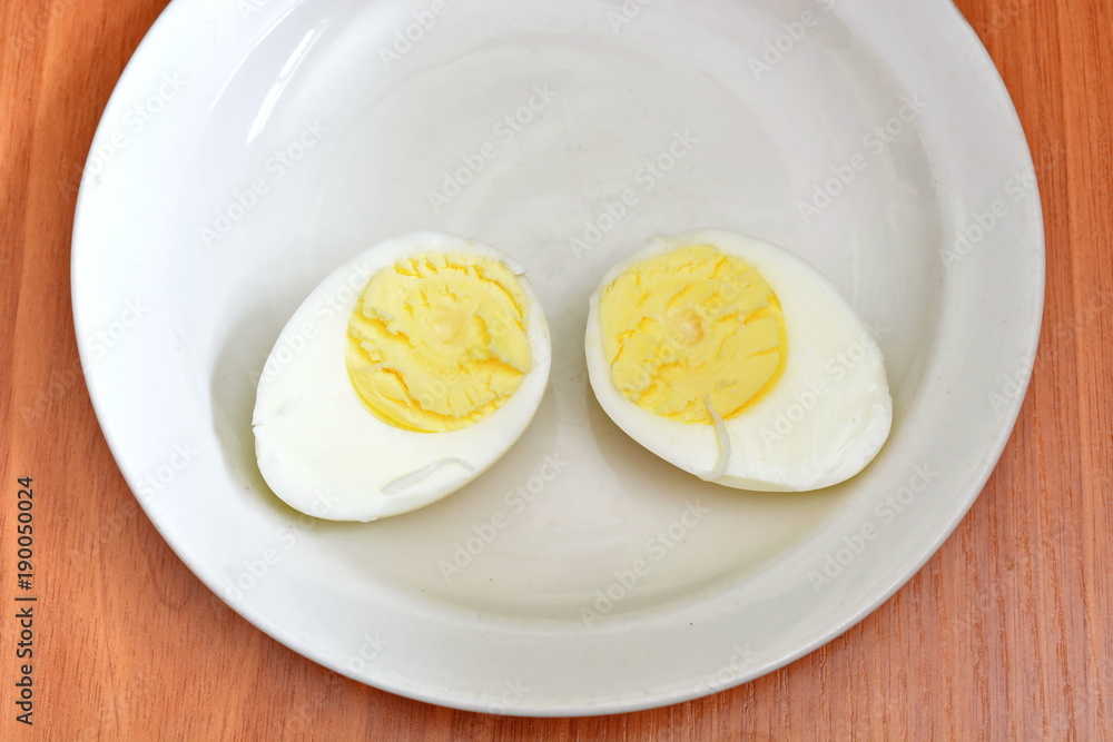 Half hard boiled chicken egg on a white saucer and wooden table Half hard boiled chicken egg on a white saucer and wooden table