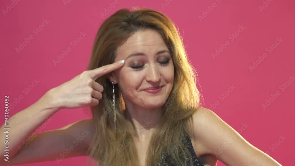 young woman gesturing with her finger against her temple. Isolated on pink background young woman gesturing with her finger against her temple. Isolated on pink background