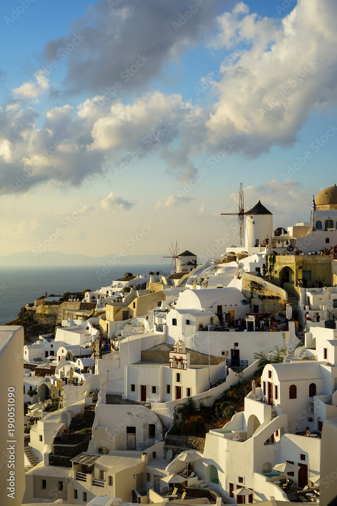 Beautiful evening light scene of Oia white building townscape along island mountain, Aegean sea, abstract cloud and blue sky background