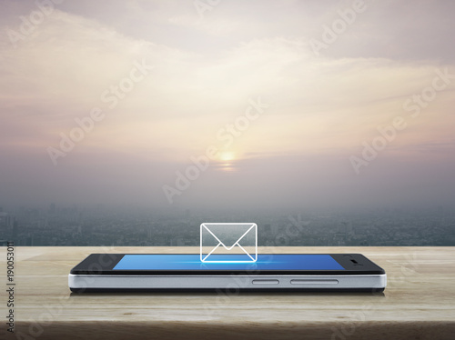email icon on modern smart phone screen on wooden table over city tower at sunset, vintage style, Business communication concept © grapestock