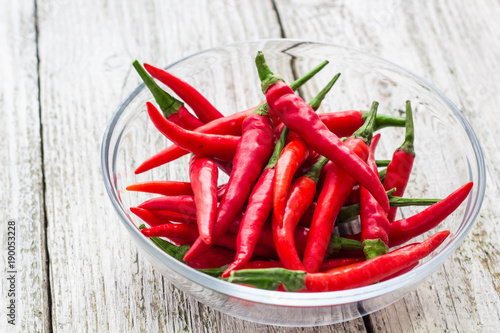 Top view Red chilli peppers in transparent bowl on white wooden background