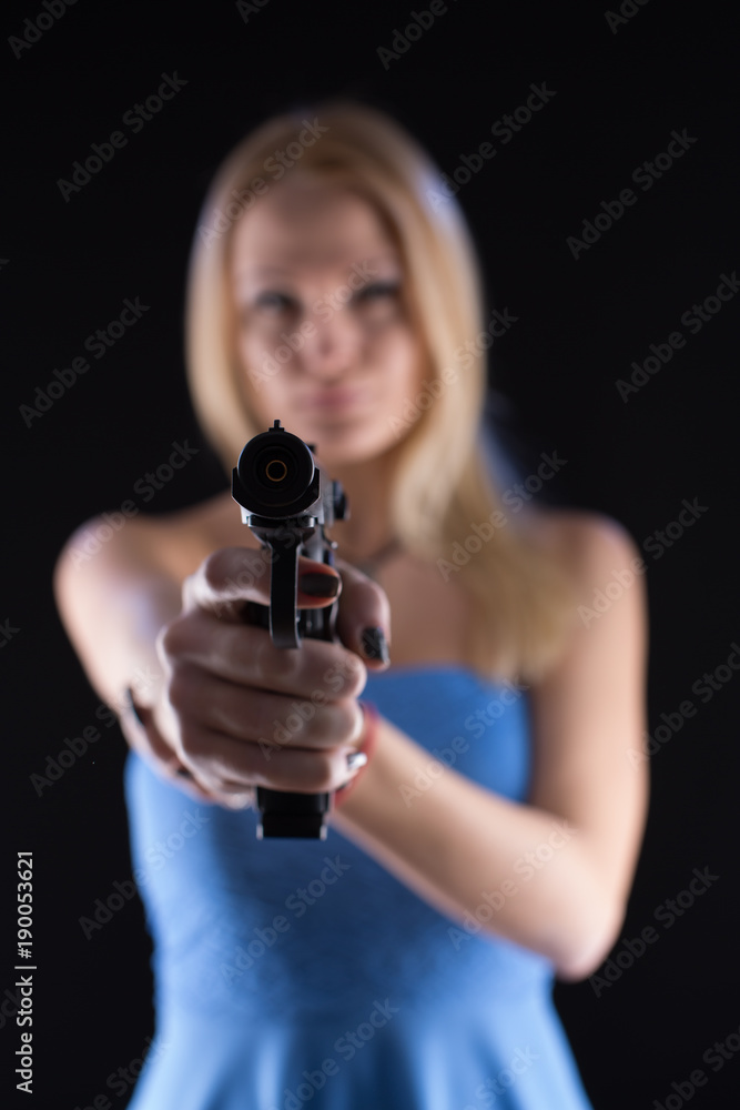 Woman in the blue dress shoots a gun on a black background Woman in the blue dress shoots a gun on a black background