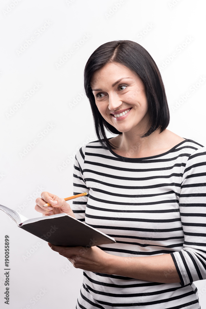 Fresh ideas. Upbeat young woman in a striped pullover smiling and making notes in her daily planner while posing against a white background Fresh ideas. Upbeat young woman in a striped pullover smiling and making notes in her daily planner while posing against a white background