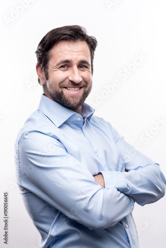 Classy look. The portrait of a handsome bearded middle-aged man in a baby blue shirt folding his arms across his chest and smiling at the camera