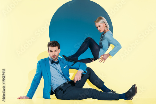 attractive stylish couple sitting and looking at camera on yellow