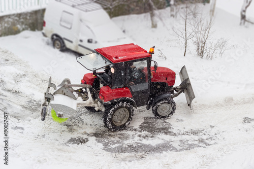 Small red tractor snow plow in courtyard during snowfall