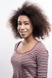 Charming smile. The portrait of a pretty young woman with curly hair, wearing a striped pullover, smiling at the camera while posing isolated on a white background