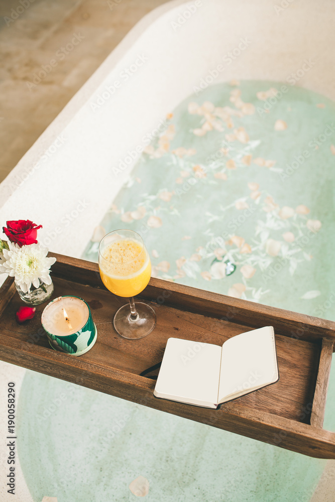 Bright Bathroom at Home. Bath with Flower Petals and Salt. Tray over the Bath with Orange Juice, Notepad and Candles.