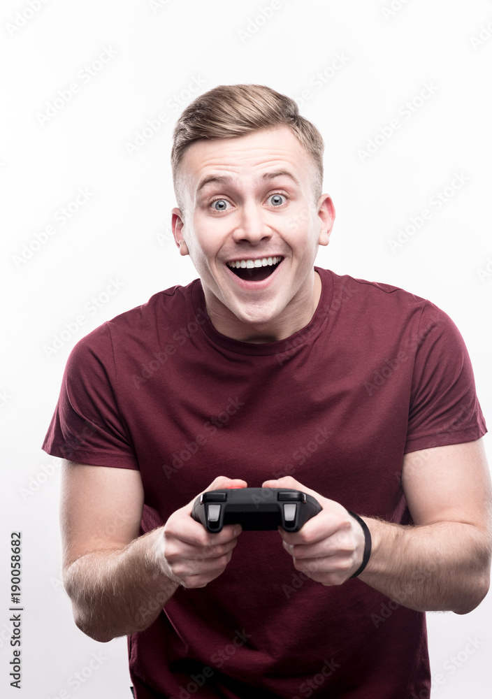 Showing nice results. Upbeat fair-haired young man holding a video game controller and smiling brightly, being excited to play a game Showing nice results. Upbeat fair-haired young man holding a video game controller and smiling brightly, being excited to play a game