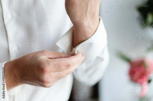 A man wears buttons of cufflinks on the sleeves of the white shirt. Businessman getting dressed by the window.
