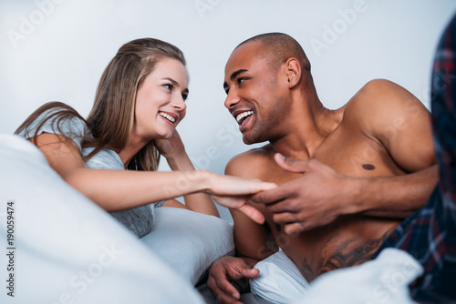 smiling multicultural couple holding hands in bed