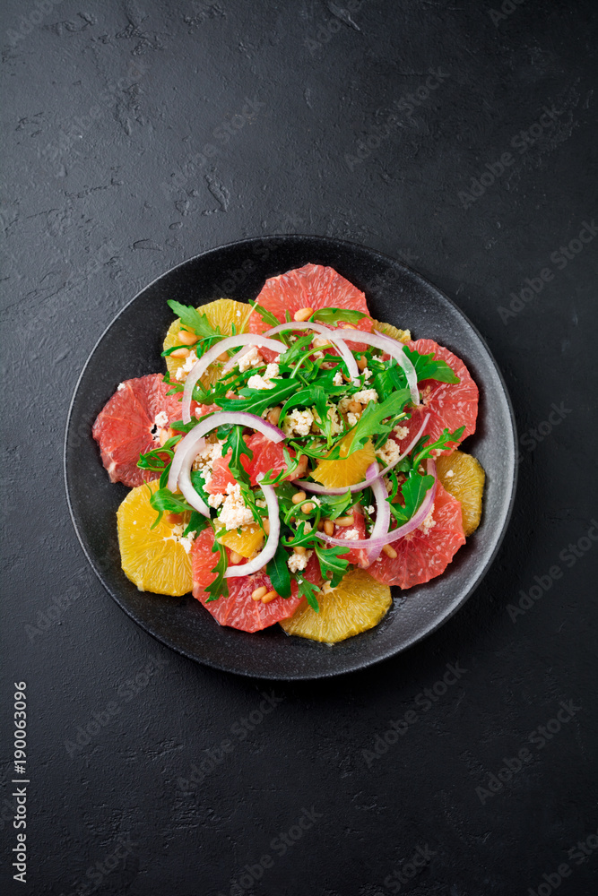Orange, grapefruit, ricotta cheese, pine nuts, red onions and arugula with olive oil in ceramic plate on gray concrete or stone old background. Selective focus. Top view. Copy space. Orange, grapefruit, ricotta cheese, pine nuts, red onions and arugula with olive oil in ceramic plate on gray concrete or stone old background. Selective focus. Top view. Copy space.