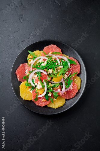  Orange, grapefruit, ricotta cheese, pine nuts, red onions and arugula with olive oil in ceramic plate on gray concrete or stone old background. Selective focus. Top view. Copy space.