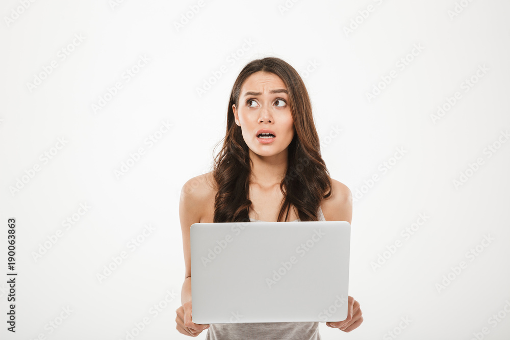 Image of young woman 30s looking away being stressed or disappointed while using silver notebook in hand, isolated over white wall Image of young woman 30s looking away being stressed or disappointed while using silver notebook in hand, isolated over white wall