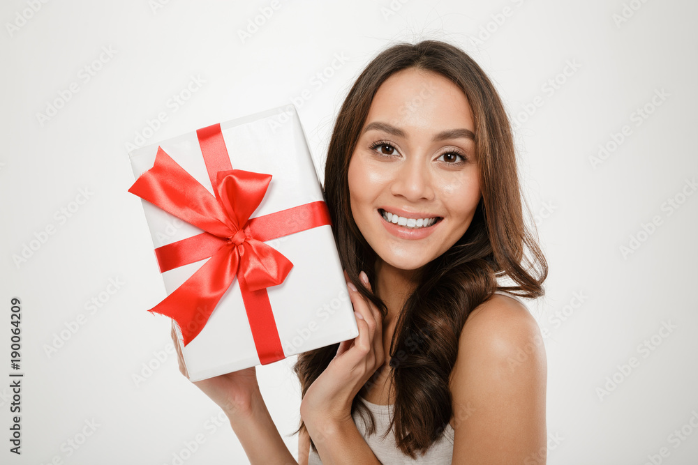 Close up photo of cheerful woman showing gift-wrapped box with red bow on camera expressing happiness and delight, isolated over white background Close up photo of cheerful woman showing gift-wrapped box with red bow on camera expressing happiness and delight, isolated over white background