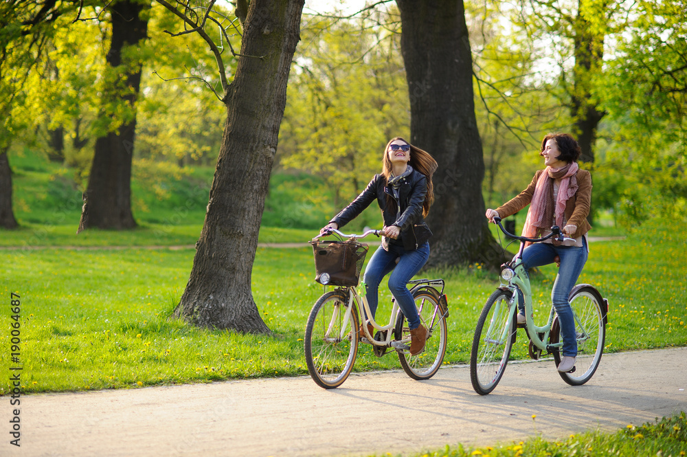 Two young attractive women ride bikes in the spring park.