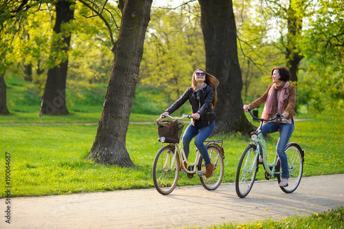 Two young attractive women ride bikes in the spring park.