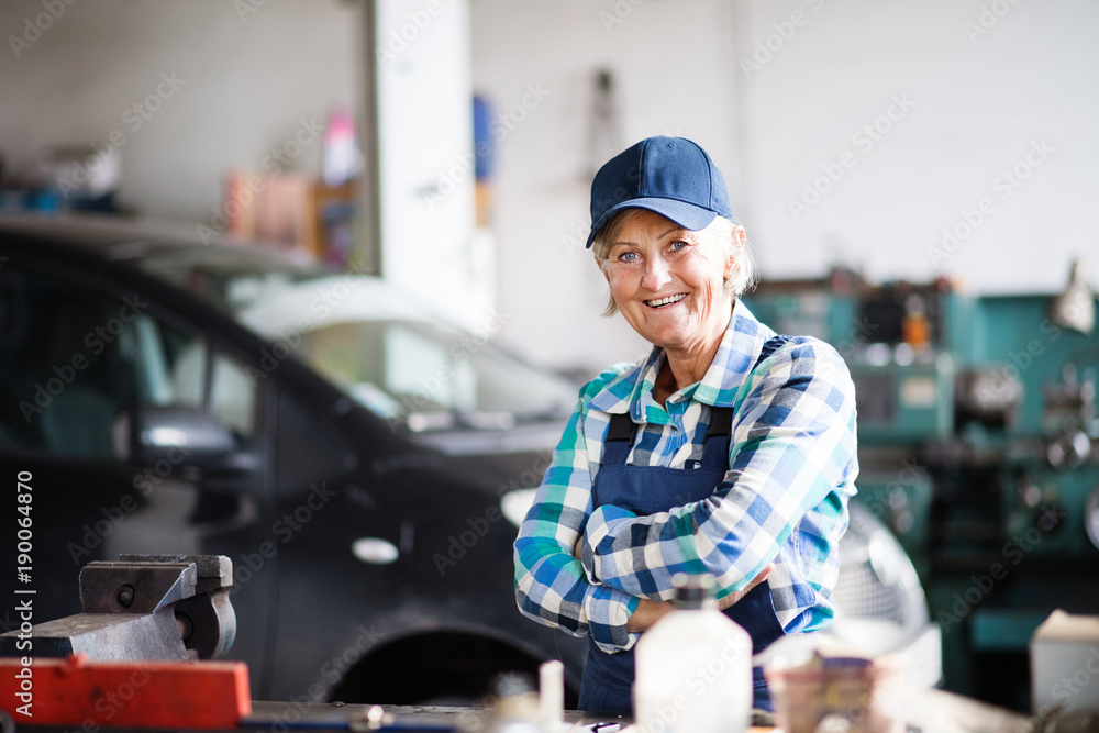 Senior female mechanic repairing a car in a garage.