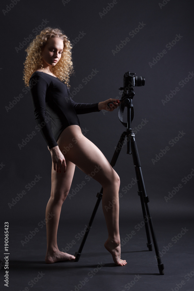 Beautiful sexy young woman in a bodysuit with a camera on a dark background. Beautiful sexy young woman in a bodysuit with a camera on a dark background.