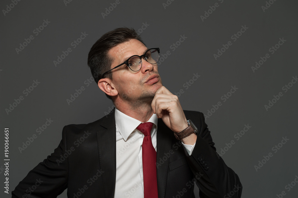 Thoughtful businessman with glasses and formal attire ponders about shares and growing exchange rate looking somewhere far away on a gray background. Copyspace Thoughtful businessman with glasses and formal attire ponders about shares and growing exchange rate looking somewhere far away on a gray background. Copyspace
