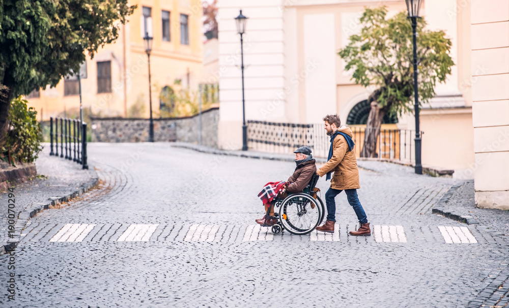 Fototapeta premium Senior father in wheelchair and young son on a walk.