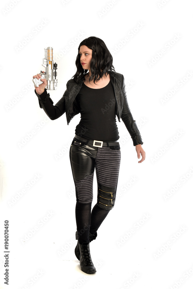 full length portrait of black haired girl wearing leather outfit. standing pose while holding a gun, isolated on a white studio background. full length portrait of black haired girl wearing leather outfit. standing pose while holding a gun, isolated on a white studio background.