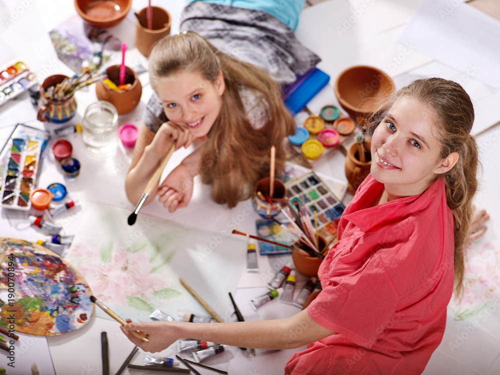 Fototapeta premium Authentic artist children girl paints with set palette watercolor paints palette and brush in morning sunlight . Painting in studio on floor.Top view indoor home interior handmade crafts .