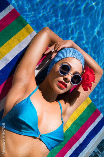 girl in a swimsuit and a swimming cap lies near the water