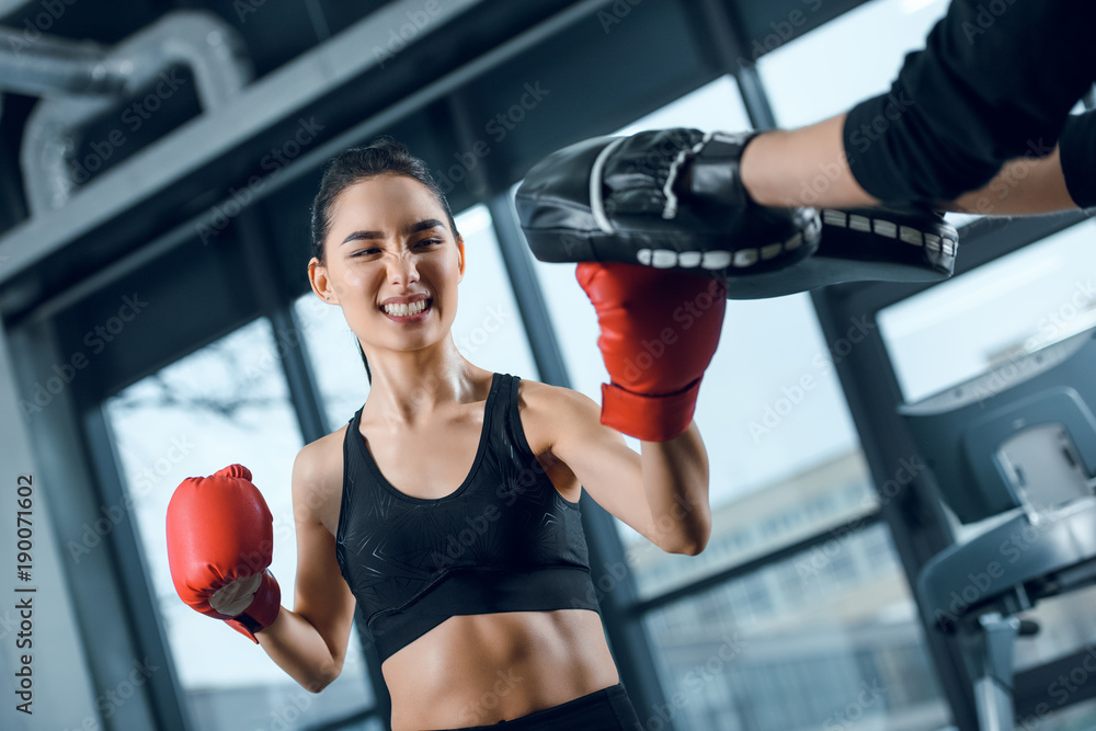 expressive young female boxer exercising with trainer at gym