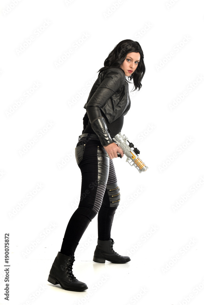 full length portrait of black haired girl wearing leather outfit. standing pose while holding a gun, isolated on a white studio background. full length portrait of black haired girl wearing leather outfit. standing pose while holding a gun, isolated on a white studio background.