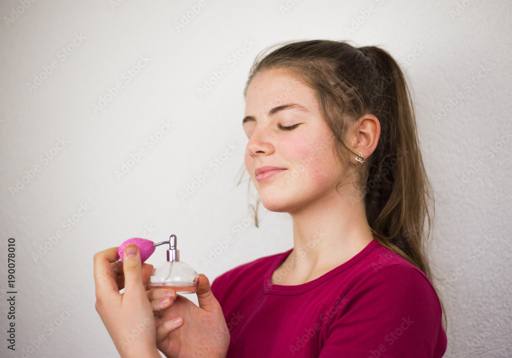 Blond teenage young kid girl putting perfume on her long neck wxposed and a head high blond hair and pink container of nice smell in the studio. Blond teenage young kid girl putting perfume on her long neck wxposed and a head high blond hair and pink container of nice smell in the studio.