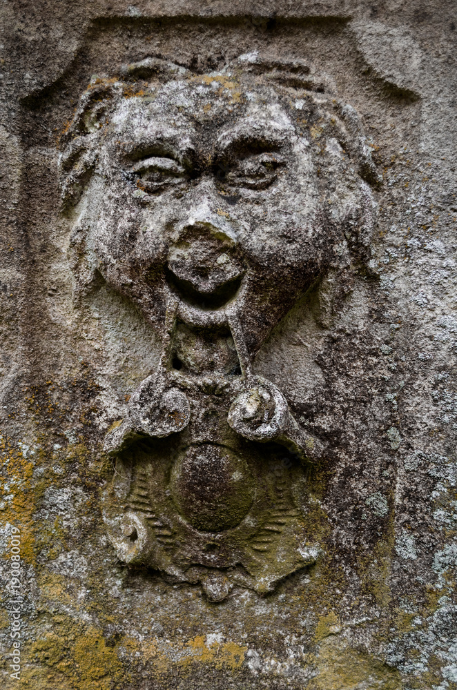 A face carved into a flat stone which has become weathered and worn A face carved into a flat stone which has become weathered and worn