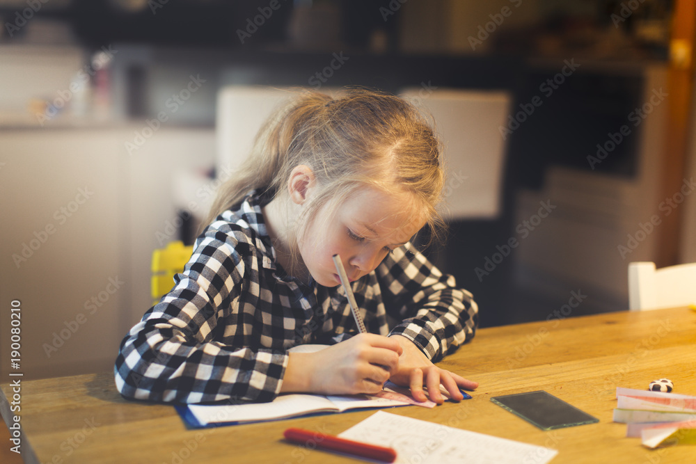 beautiful, blond girl is sitting at the table and is doing schoolwork at home beautiful, blond girl is sitting at the table and is doing schoolwork at home
