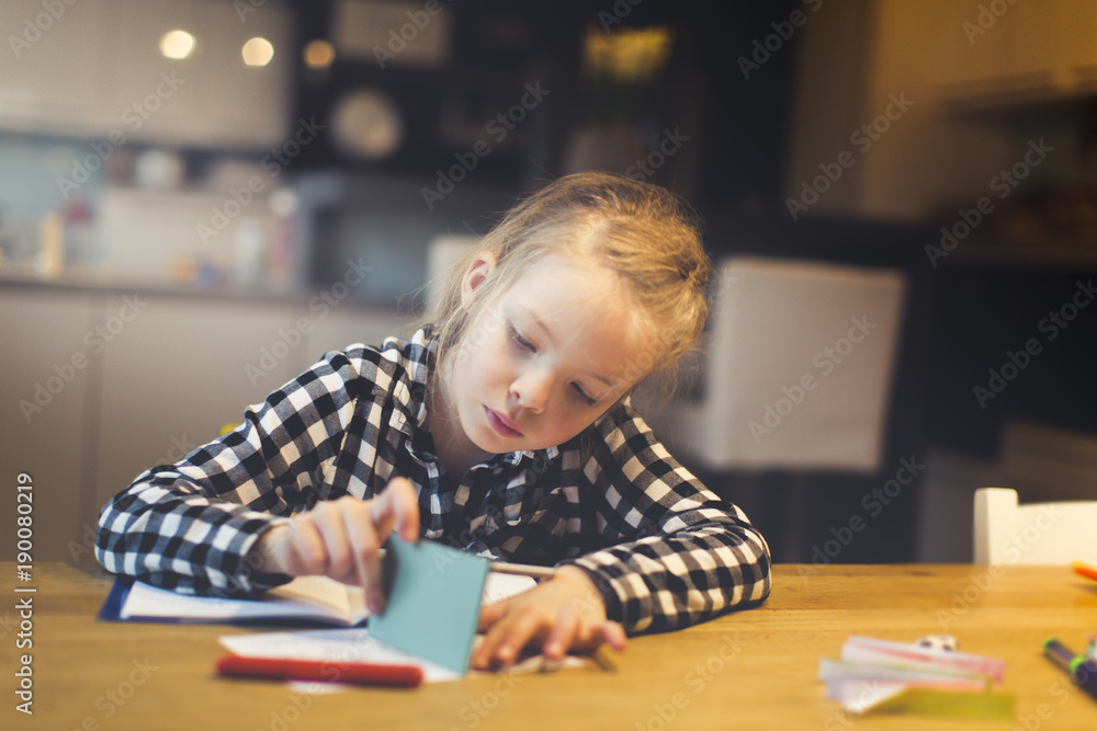 beautiful, blond girl is sitting at the table and is doing schoolwork at home beautiful, blond girl is sitting at the table and is doing schoolwork at home